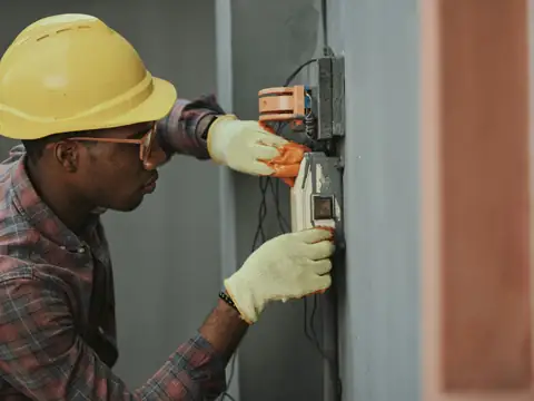 An electrician in a hard hat working on a wall panel