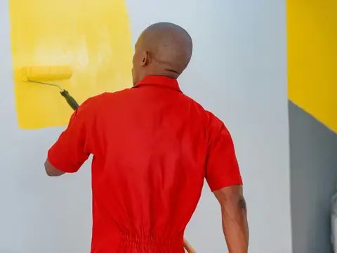 A painter rolling yellow paint onto a wall