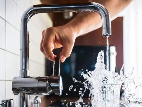 A hand adjusting a kitchen mixer tap with water splashing