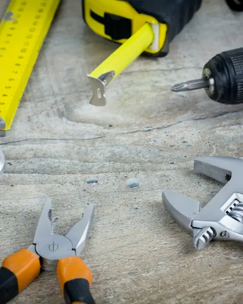 A tape measure, spanners, pliers and a drill laid out on a wooden table